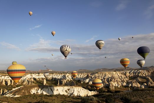 Cappadocia, Turkey: June 2011 - skies over Kapadokya filled with colorful hot air balloons, blue sky, wispy clouds, mountain landscape and rough terrain