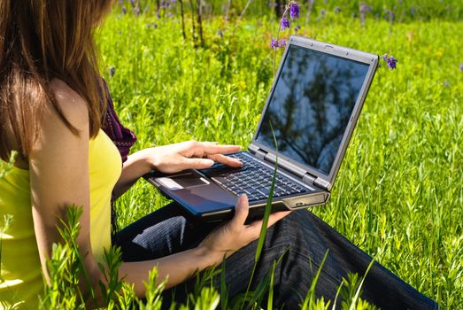 Young woman working on laptop outdoor. Sunny summer day.