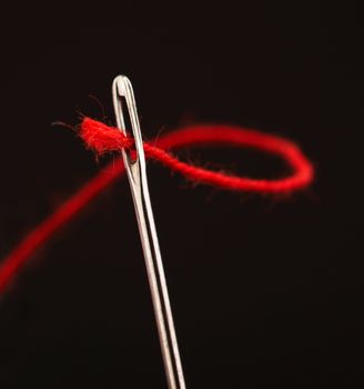 Red thread going through needle eye, closeup