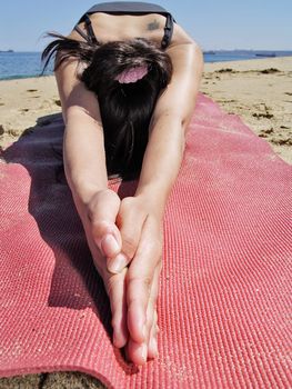 Yoga teacher practising at the beach pose ardha kurmasana