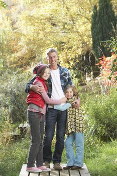 Father And Children Standing Outdoors On Wooden Walkway In Autum