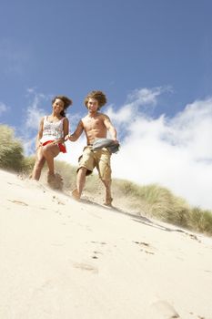 Young Couple Running Down Sand Dune On Beach