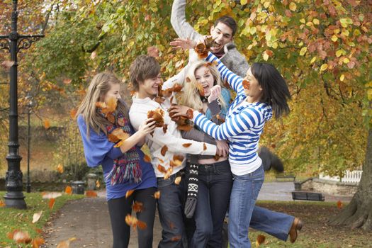 Group Of Teenage Friends Throwing Leaves In Autumn Landscape