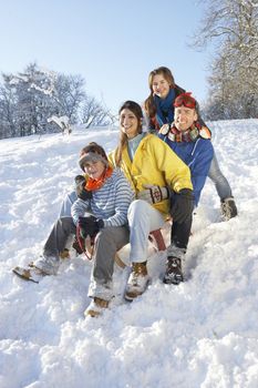 Family Enjoying Sledging Down Snowy Hill