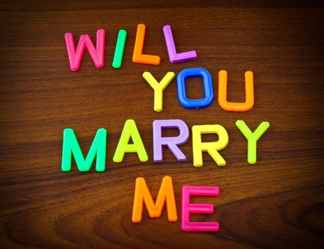 Will you marry me in colorful toy letters on wood background