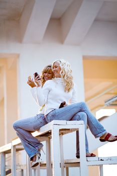 Two teenage girls sit and talking watching mobile phone.