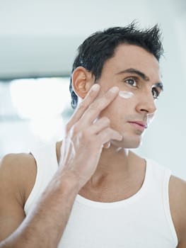 young caucasian man applying eye cream on face. Vertical shape, front view, waist up