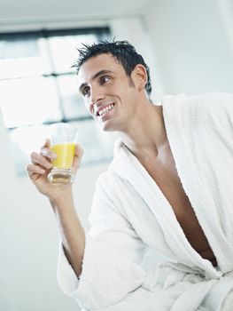 adult caucasian man in white bathrobe drinking orange juice. Vertical shape, waist up, side view