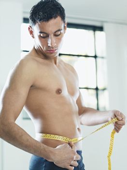 caucasian young man measuring waist with yellow tape. Vertical shape, waist up, side view, copy space