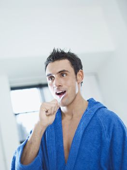 caucasian adult man with bathrobe brushing teeth in bathrooom. Vertical shape, waist up, copy space