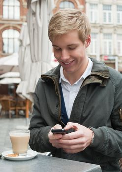 Young blond handsome smiling man typing a text message on his mobile phone