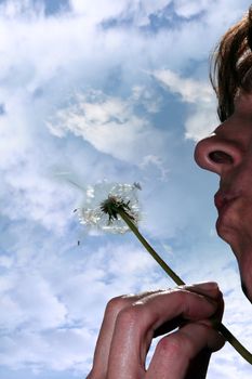 a beautiful dandelion being gently blown by a middle aged woman in a garden against a cloudy sky
