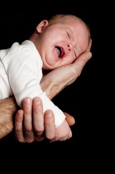 a fathers hand is holding a crying newborn baby