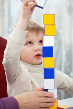Little blond boy is building tower from colorful blocks