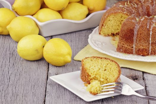 Slice of moist lemon bundt cake with real lemons in background. Shallow depth of field.