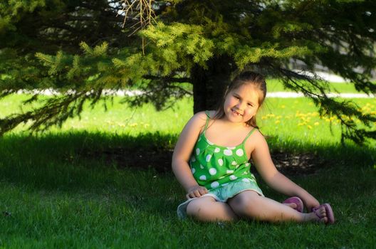A young girl sitting in the shade of a tree is smiling.