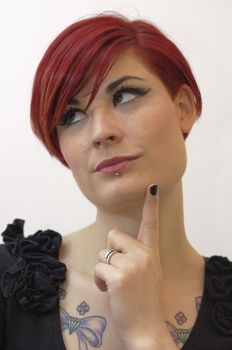 Portrait of a girl with red hair, piercing on lower lip, and tattoos on chest and shoulders, thinking expression.