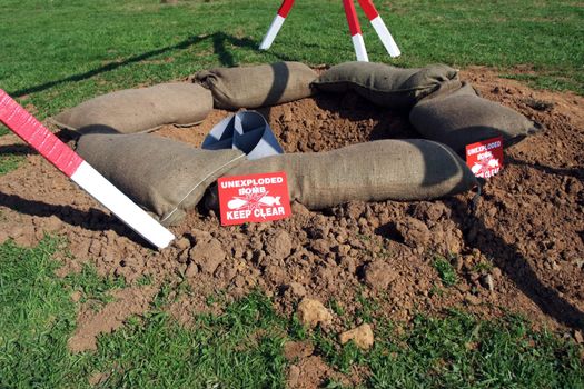 An unexploded bomb in a crater with warning signs. A set from the Second World War