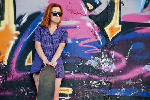 Style girl with skateboard near graffiti wall.