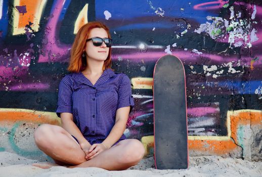 Style girl with skateboard near graffiti wall.