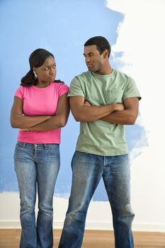 African American couple glaring at each other with anger next to half-painted wall.