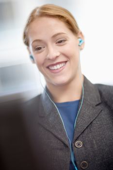 Young office worker with earbuds smiling as she looks at computer screen