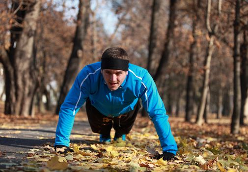 Man doing push-ups outdoor in a park in autumn.