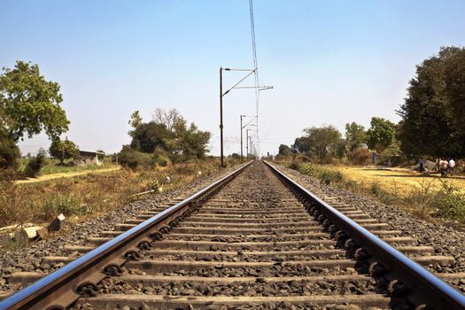 landscape of railroad tracks in Indian cutting across the rural countryside along the outskirts of o Gujarat village near the city of Surat. Typical scenec with litter thrown around and locals walking close by
