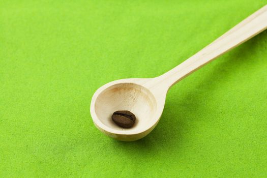 coffee beans in a wooden spoon on a green background