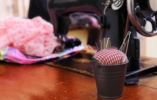 Image of an old-fashioned tailoring table.The selective focus is on the little pail with the pin-cushion.