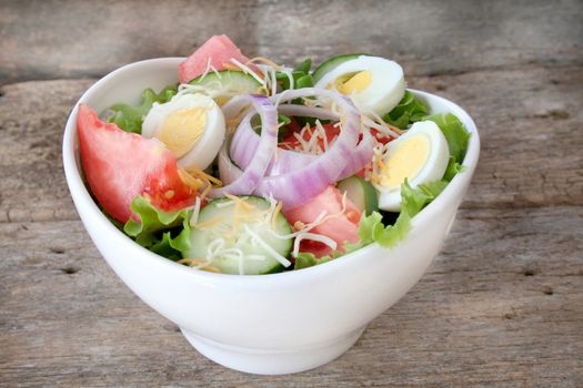Fresh salad with all the fixings in a white bowl and a rustic looking background.