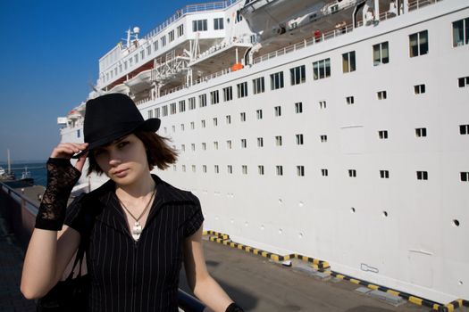 Stylish tourist girl in black hat near the passenger ship 