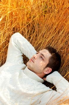 Autumn winter man portrait lying in golden grass field with turtleneck sweater