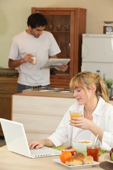 a woman having breakfast, her husband is reading newspaper