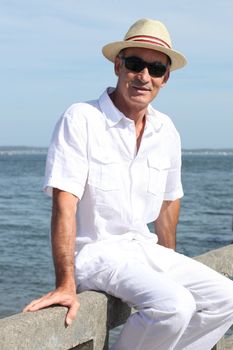 Elderly man sitting on a wall by the sea
