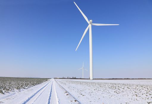 Image of a small road between  wind turbines in a plain covered by snow in winter.
