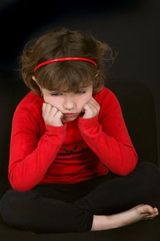 little girl pouting with face resting on hands against black background