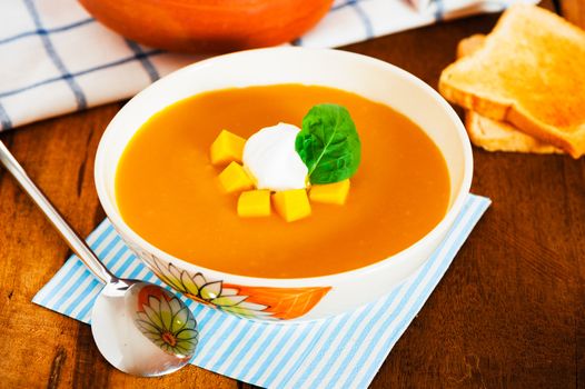 Pumpkin soup with cream in a bowl with painted flower and toast 