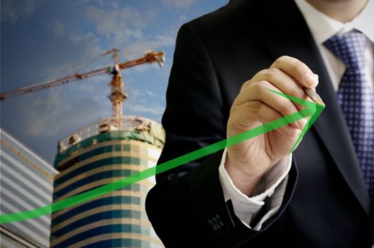 Businessman write a grow up green arrow with construction site background
