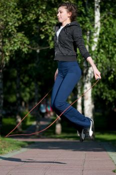 Beautiful young woman doing  exercise with skipping rope at park. Jumping