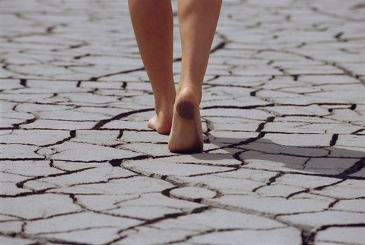 Woman walking barefoot across cracked earth, low section