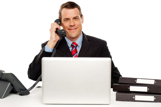 Male executive communicating with client on telephone and feeding instruction on laptop