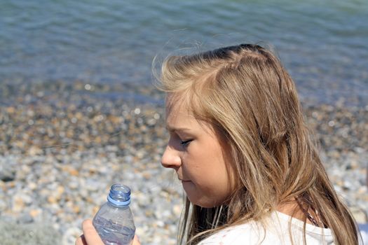 teenage girl drinking water sat on a beach