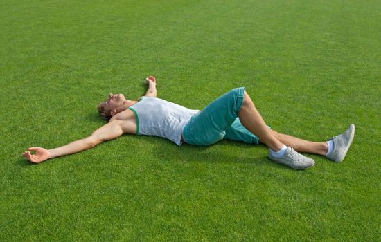 Sporty guy relaxing on green training field