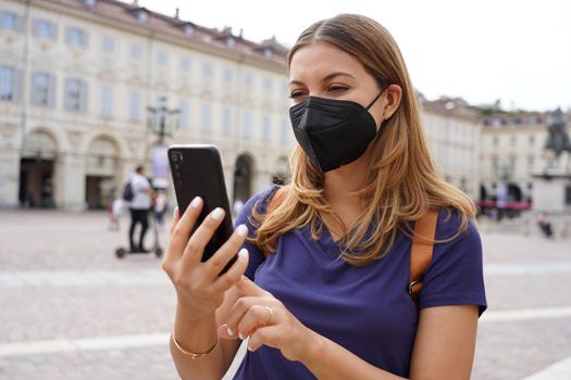 Portrait of young woman with black protective mask FFP2 KN95 using mobile phone with city background