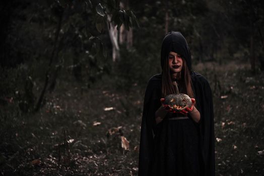 Woman horror ghost holding reaper and pumpkin inn forest