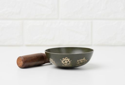 Tibetan singing copper bowl with a wooden clapper on a white wooden table, objects for meditation and alternative medicine