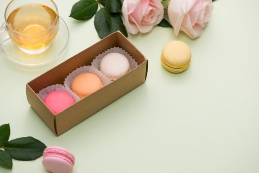 French macaroons. Many variegated sweet macarons in box with bouquet of pink roses on the table