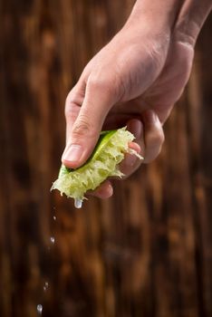 Hand squeeze lime with lime drop on dark wooden background