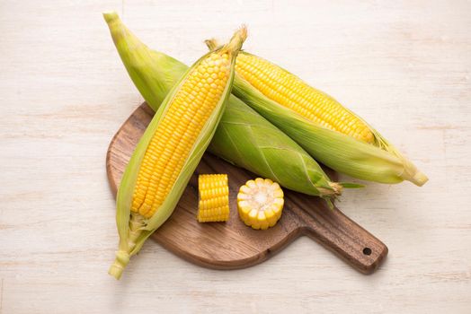 Sweet corn on cobs on cutting board on wooden table.